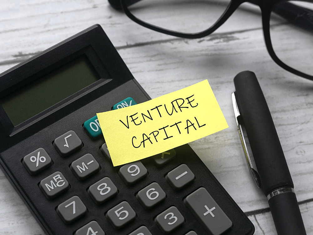Venture Capital: imagem de uma calculadora em cima de uma mesa com um post it amarelo escrito venture capital