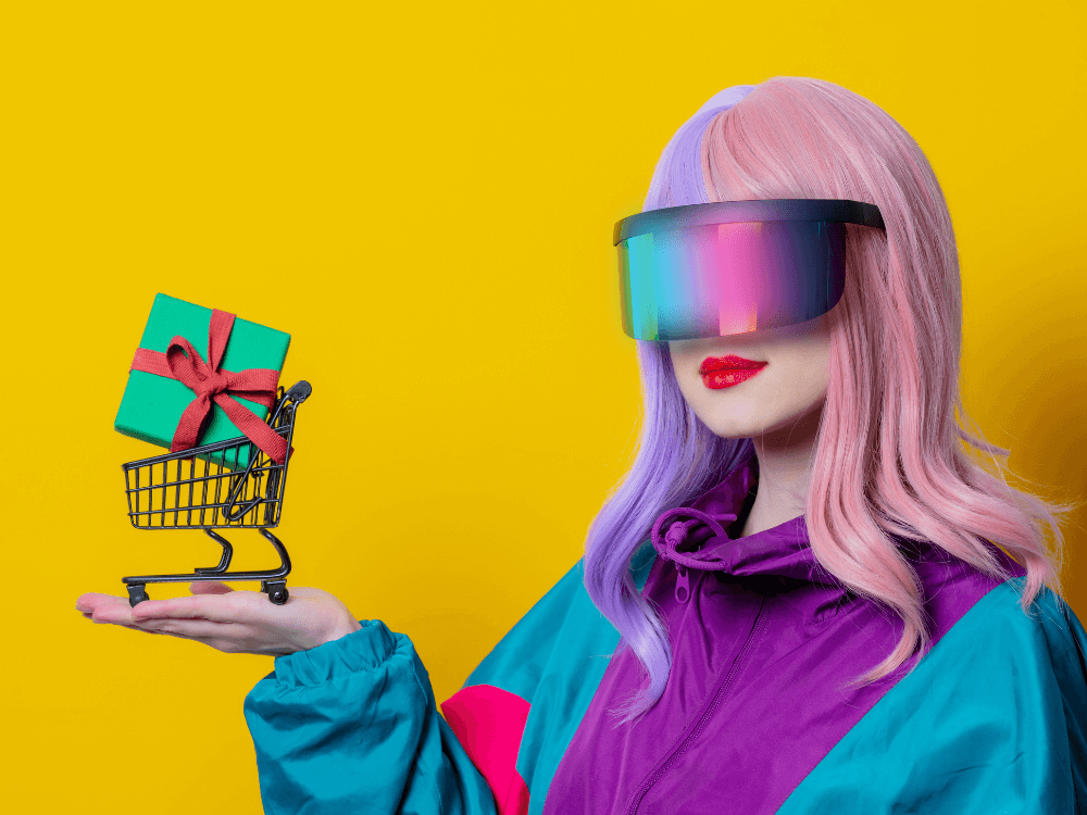 e-commerce no brasil: tendências para 2022. Imagem de mulher com cabelo rosa, óculos no estilo VR e corta-vento roxo e verde segurando um carrinho miniatura com uma caixa de presente na cor verde dentro. Fundo amarelo.