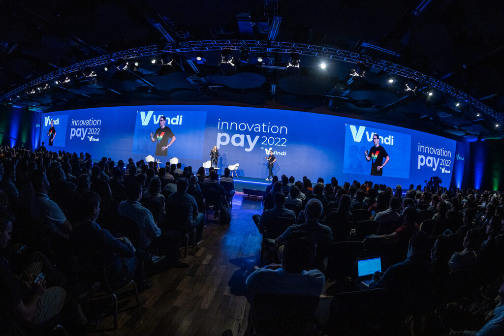 Innovation Pay 2022: imagem do palco com luz azul e plateia na sombra. Rodrigo Dantas e Rafa Brites no centro
