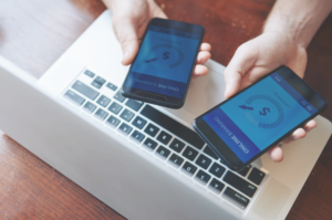 Modernizar formas de pagamento. Imagem de duas pessoas segurando celulares perto de notebook. Nas telas estão os textos: Online Banking e um sinal de espera da transferência.